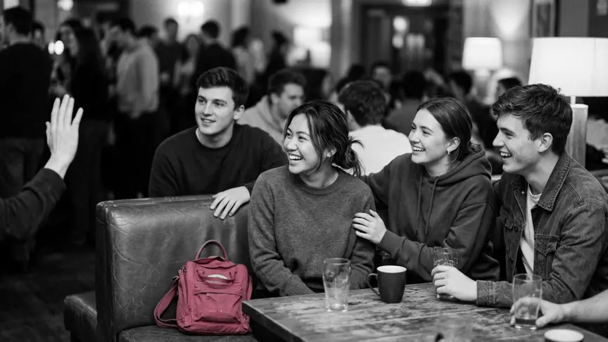 En un bar d’associació d’estudiants ple de gent, un vespre entre setmana, una noia d’uns vint anys seu atapeïda en un reservat amb tres amics de la seva edat, i riu mentre un d’ells l’empeny cap a un noi a l’altra banda de la sala que l’acaba de saludar amb la mà. Tothom porta roba normal d’estudiant — dessuadores llises, samarretes llises, texans amples, vambes, sense lletres ni logotips enlloc —, i al seient del costat té deixada una bossa de tela llisa de color rosa intens, sota una llum càlida i tènue, amb un ambient de discreta esperança.